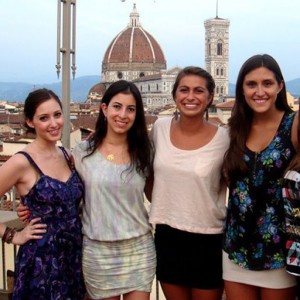 4 women on a balcony in Florence, Italy, with The Basilica di Santa Maria del Fiore in the distance.