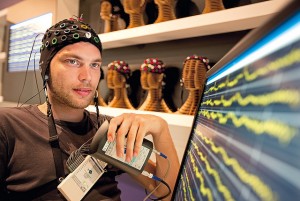 Image of a man wearing a cap of electrodes and looking at his brain activity on a monitor