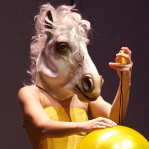 Micol Hebron in a yellow dress and wearing a horse head mask