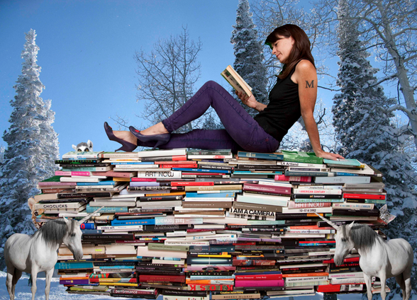 Micol Hebron seated on top of a giant pile of art and theory books. She relaxes and reads a book.